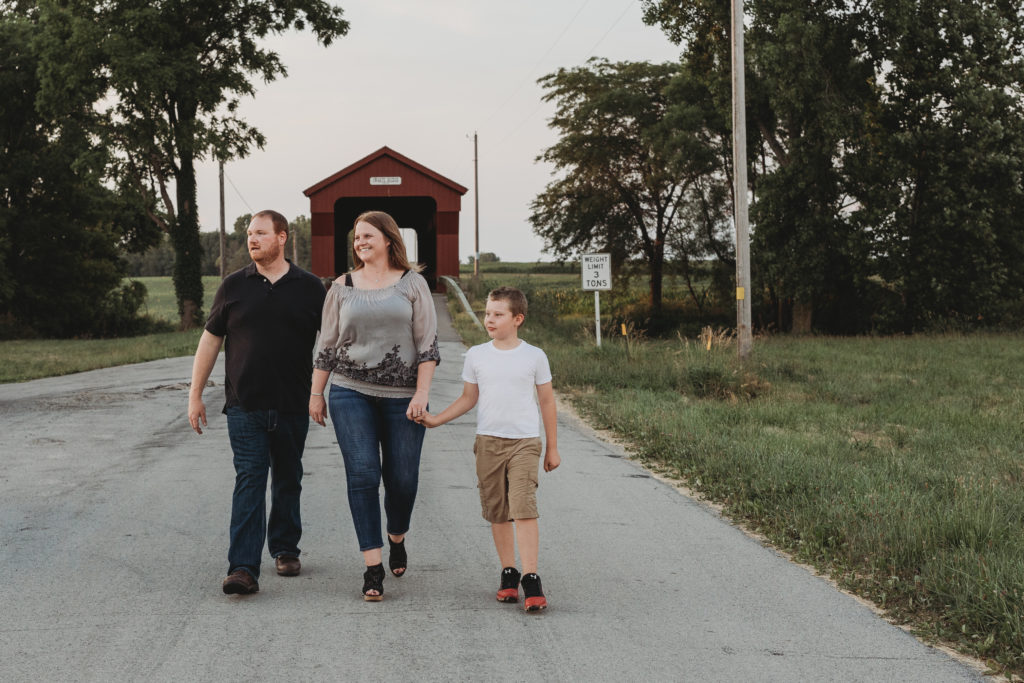 Brandon, Rachel, and Rachel's Son are walking down the road, holding hands with the Swartz Covered Bridge behind them.