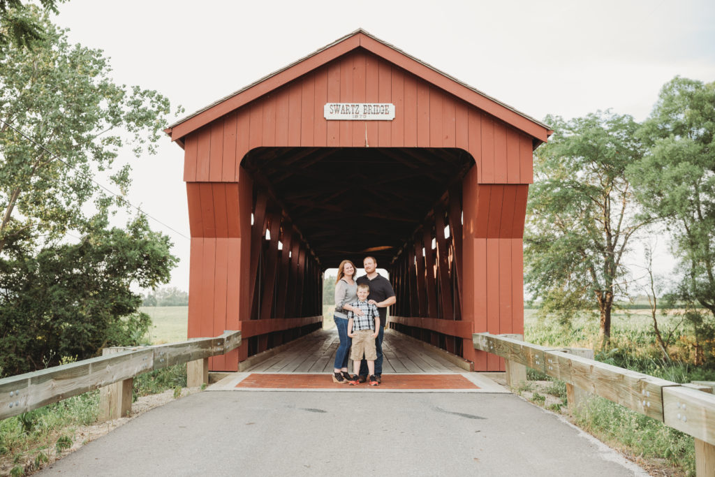 Family of 3 stand just outside the entrance to the Swartz Covered Bridge.